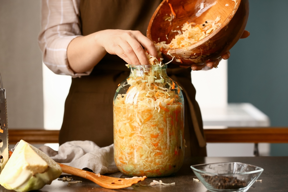 Woman,Putting,Tasty,Sauerkraut,Into,Glass,Jar,On,Table,In